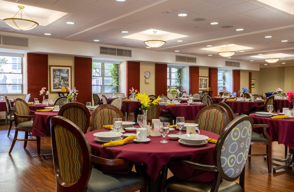 The large dining hall at Celebrate Senior Living with round tables with a well-laid table.